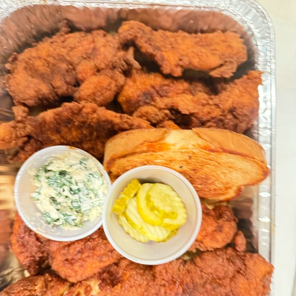 Mr Feast Hot Chicken tenders in a foil pan with coleslaw, pickles, and toast.