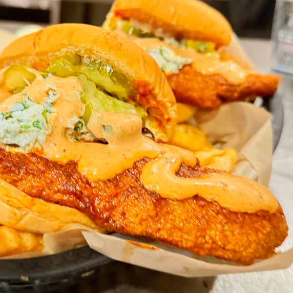 Two Mr Feast Hot Chicken sandwiches with pickles, slaw, and spicy sauce, served with fries.