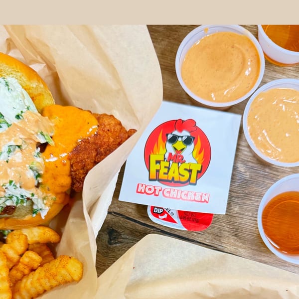 Mr Feast Hot Chicken sandwich with fries, sauces, and branded packaging on a wooden table.