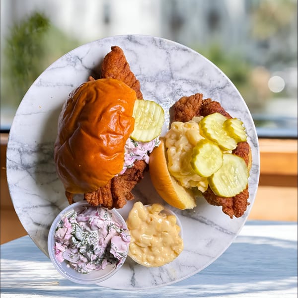 Two Mr Feast Hot Chicken sandwiches, one with coleslaw and one with mac and cheese, on a marble plate.