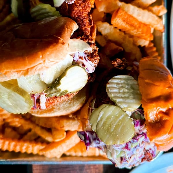Two Mr Feast Hot Chicken sandwiches with pickles and slaw, surrounded by crinkle-cut fries.