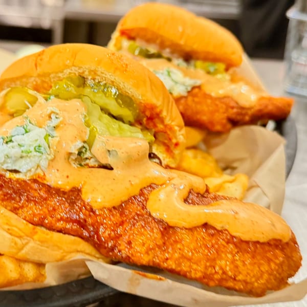 Two Mr Feast Hot Chicken sandwiches with pickles, slaw, and sauce, served with fries.