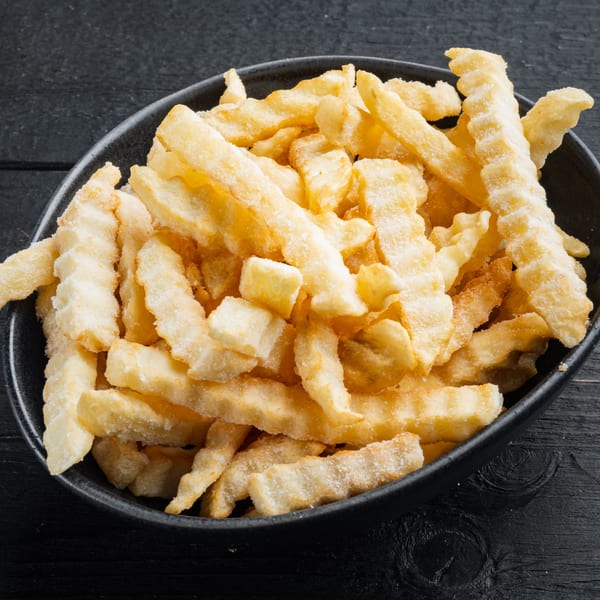 A black bowl filled with golden, crinkle-cut french fries, lightly salted, on a dark wooden surface.